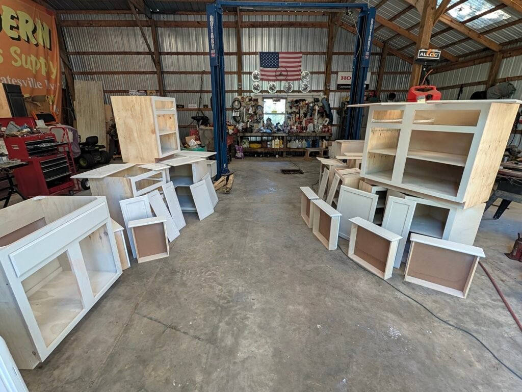 Staging unfinished oak kitchen cabinets with plywood boxes across a workshop floor for spray painting